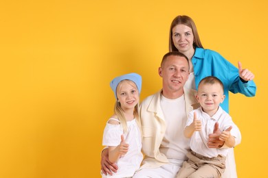 Photo of Family portrait of parents and their children showing thumbs up on yellow background. Space for text