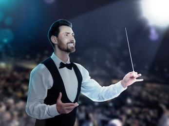 Image of Conductor directing orchestra with baton on stage of concert hall