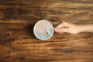 Image of Woman holding cup with ocean beach inside at wooden table, top view