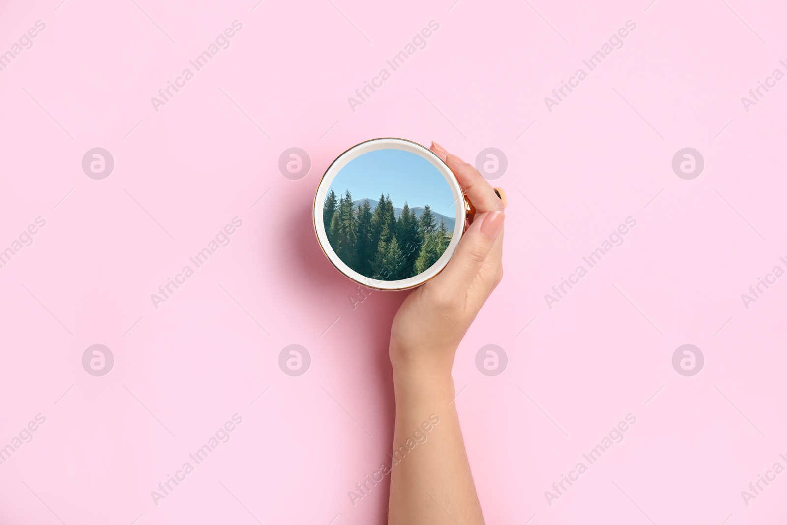 Woman holding cup with mountain landscape inside on pink background, top view Image of Woman holding cup with mountain landscape inside on pink background, top view