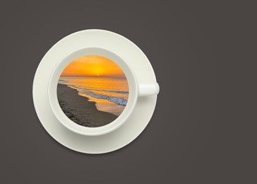 Image of Ocean waves rolling onto sandy beach at sunset inside cup on dark grey background, top view