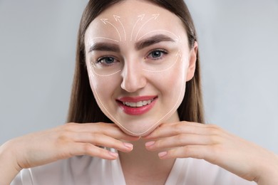 Image of Beautiful woman with perfect skin after collagen treatment on grey background. Arrows on her face illustrating lifting and smoothing effect