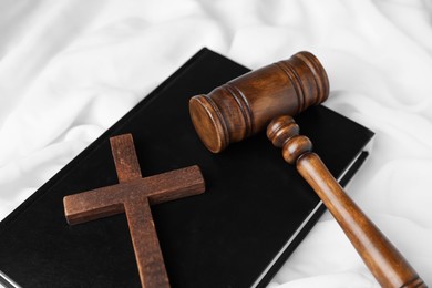Photo of Judge's gavel, Bible and wooden cross on white fabric, above view