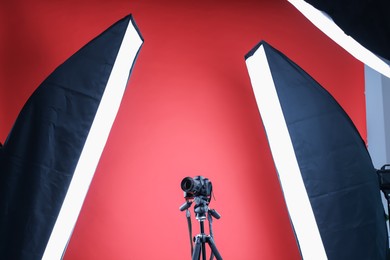 Photo of Modern video camera and professional lighting equipment on red background, low angle view