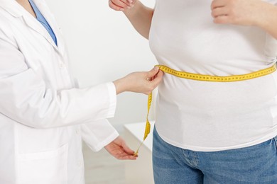 Photo of Weight loss. Nutritionist measuring overweight woman's waist with tape in clinic, closeup