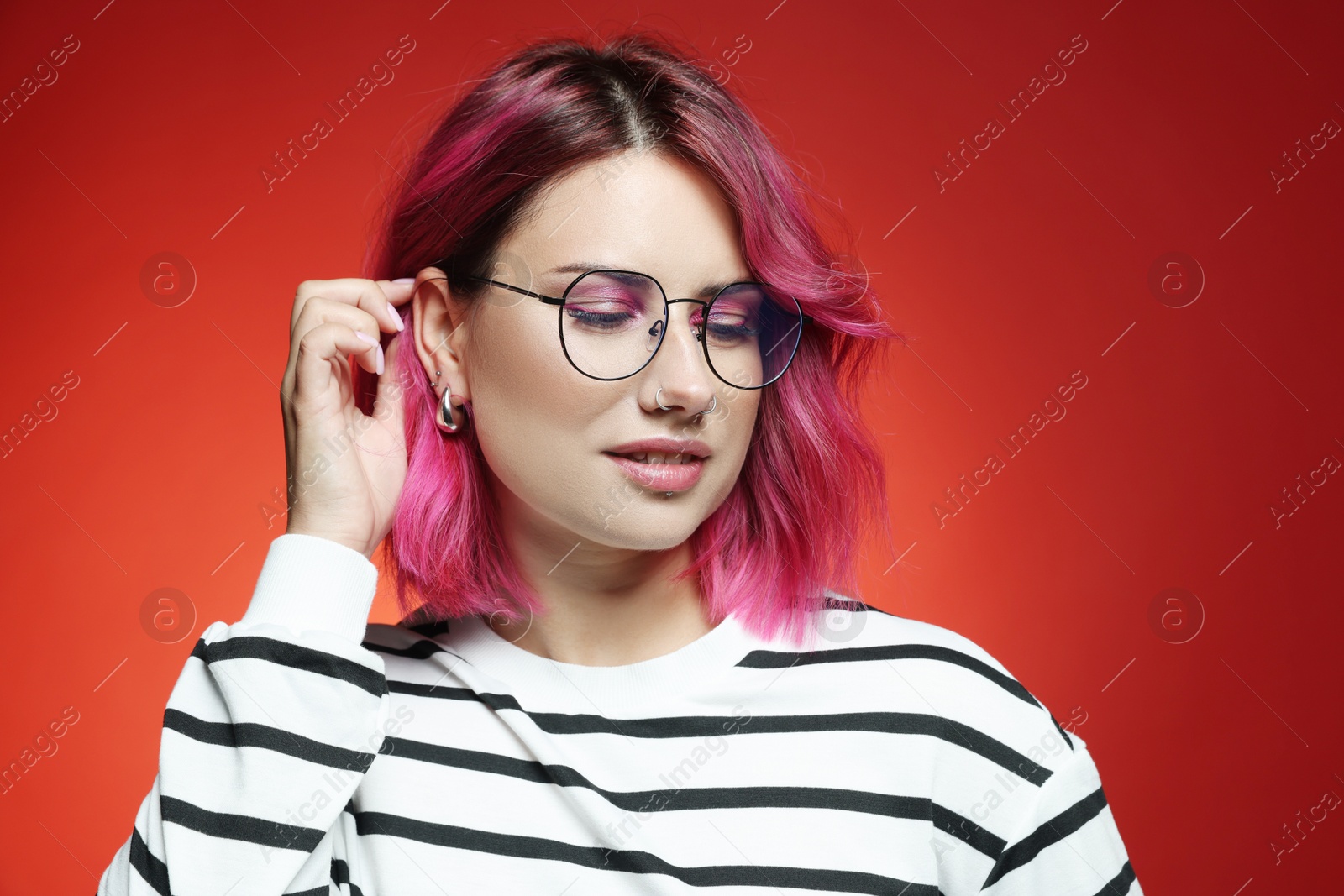 Beautiful woman with pink dyed hair in glasses on red gradient background Photo of Beautiful woman with pink dyed hair in glasses on red gradient background