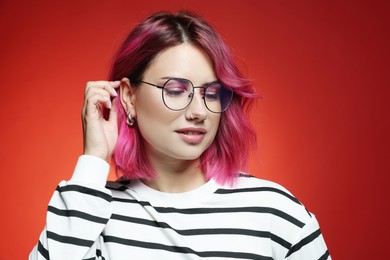 Photo of Beautiful woman with pink dyed hair in glasses on red gradient background