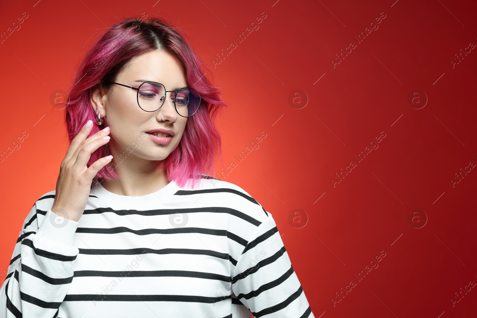 Beautiful woman with pink dyed hair in glasses on red gradient background, space for text Photo of Beautiful woman with pink dyed hair in glasses on red gradient background, space for text