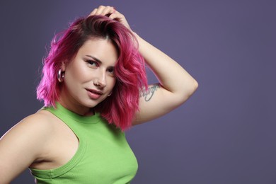 Photo of Beautiful woman with pink dyed hair on violet background, space for text