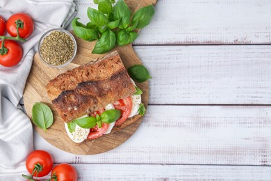 Photo of Tasty sandwich with mozzarella cheese, tomatoes and basil on white wooden table, flat lay. Space for text