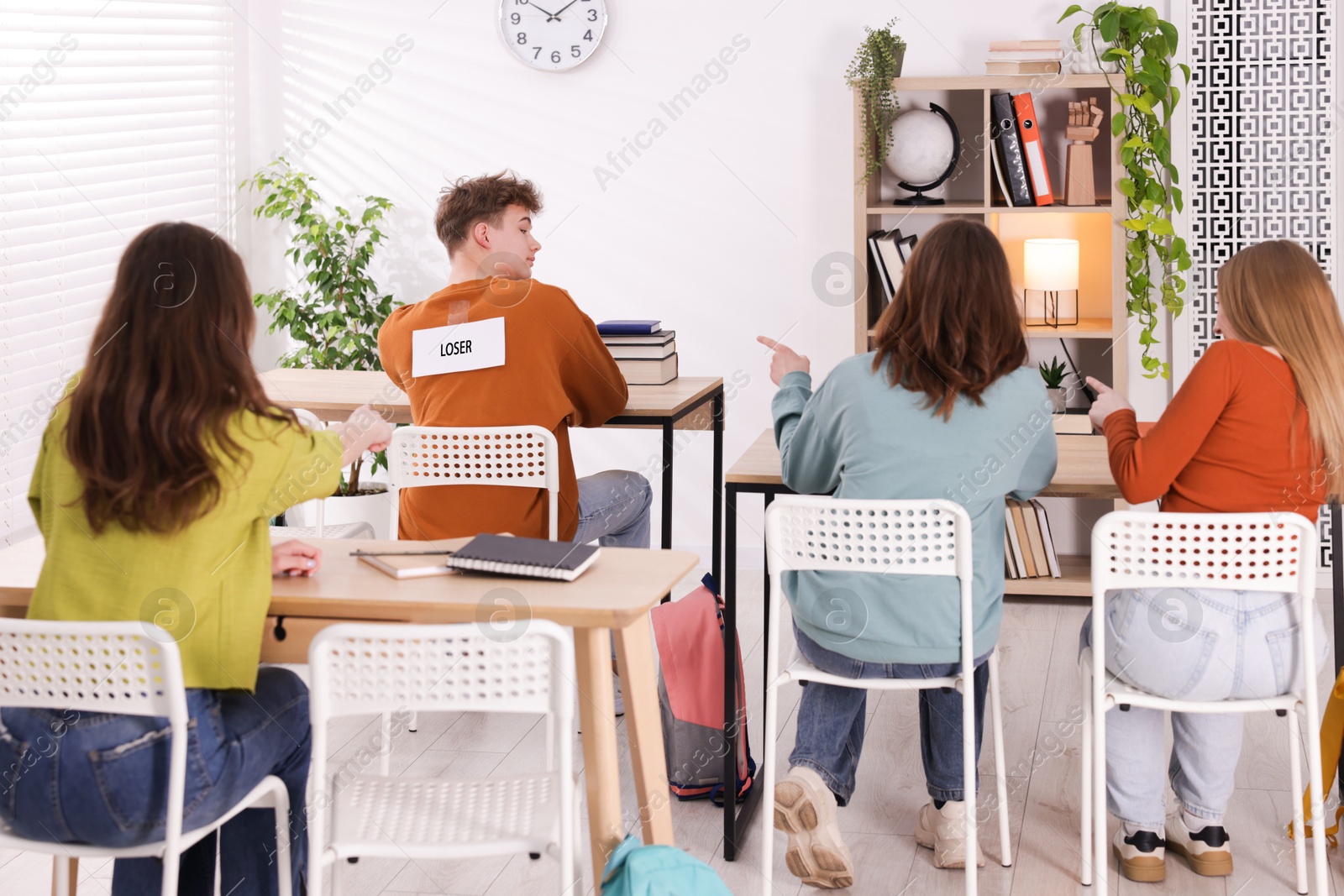 Photo of Schoolmates bullying teenage boy with sign You Loser on his back at school