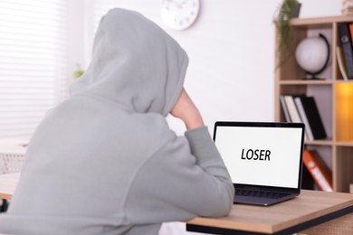 Photo of Cyber bullying. Upset teenage girl and laptop with text You Loser at desk indoors