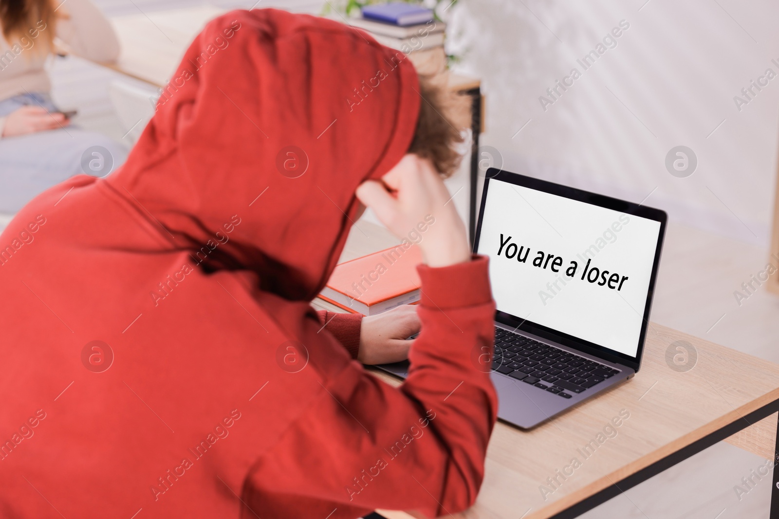 Cyber bullying. Upset teenage boy and laptop with text You Loser at desk indoors, closeup Photo of Cyber bullying. Upset teenage boy and laptop with text You Loser at desk indoors, closeup