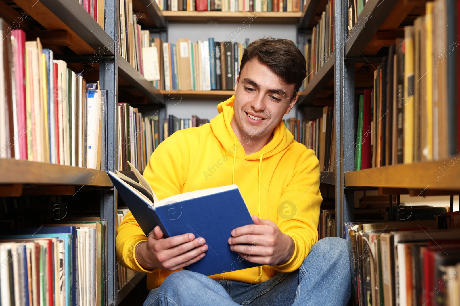Man reading book near shelves in public library Photo of Man reading book near shelves in public library