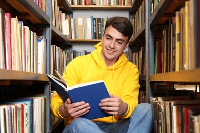 Photo of Man reading book near shelves in public library