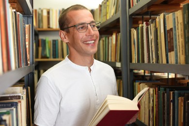 Photo of Man with book near shelves in public library