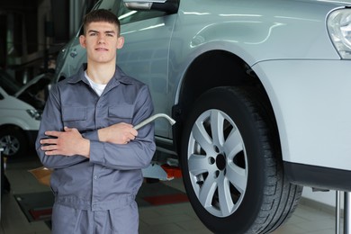 Photo of Professional mechanic with wrench near lifted car in garage