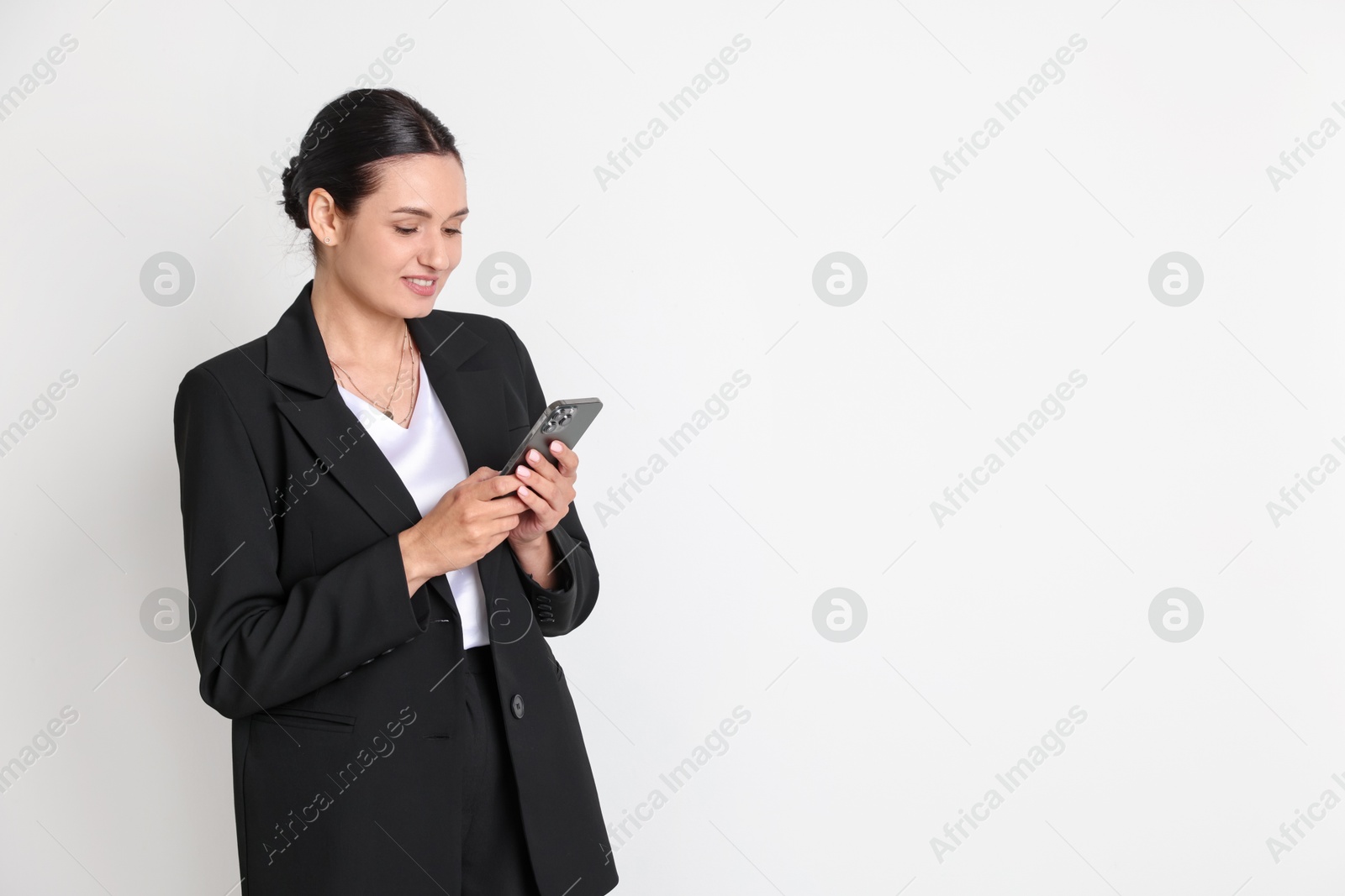 Confident business woman in suit with smartphone on light background. Space for text Photo of Confident business woman in suit with smartphone on light background. Space for text