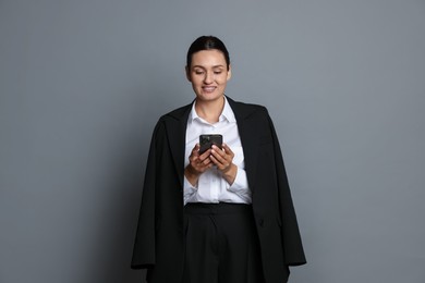 Photo of Confident business woman in suit with smartphone on grey background