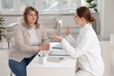 Photo of Weight loss. Nutritionist consulting overweight woman at white desk in clinic