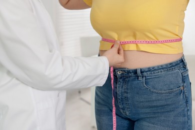 Photo of Weight loss. Nutritionist measuring overweight woman's waist with tape in clinic, closeup