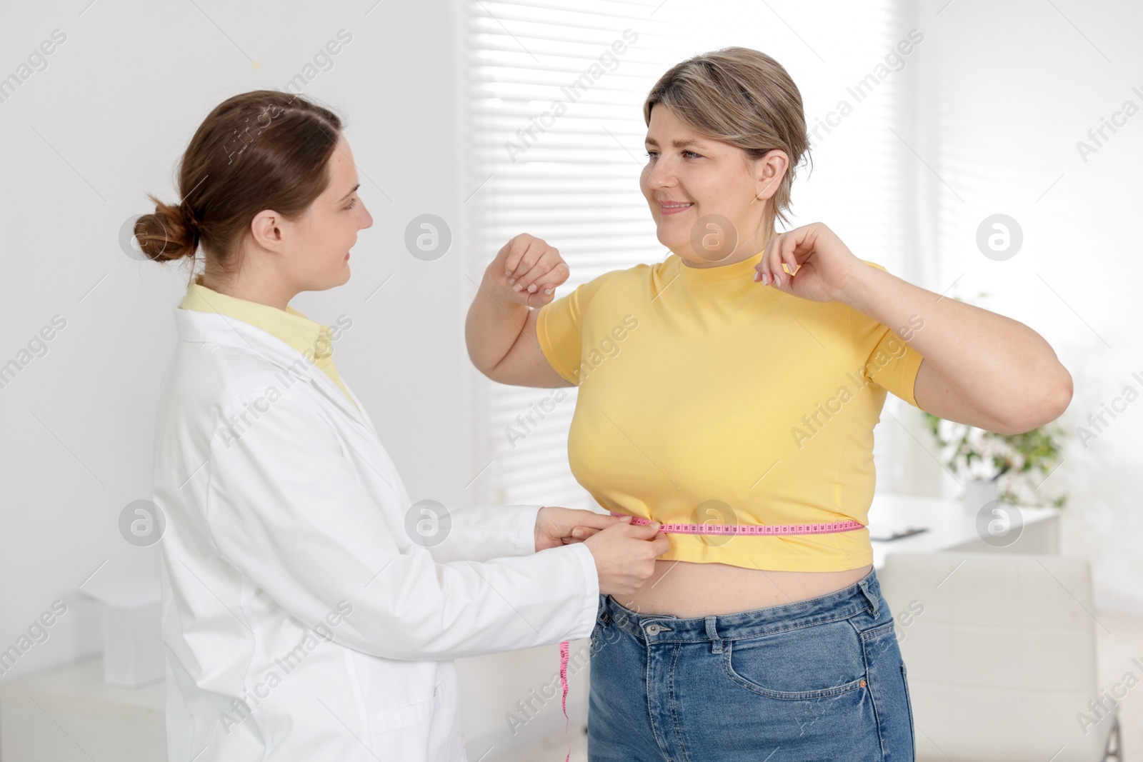 Weight loss. Nutritionist measuring happy overweight woman's waist with tape in clinic Photo of Weight loss. Nutritionist measuring happy overweight woman's waist with tape in clinic