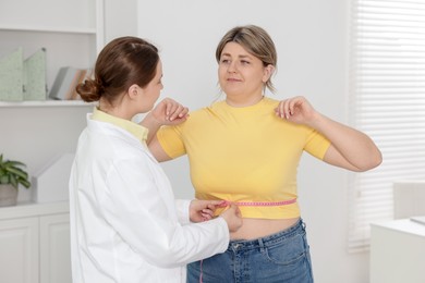 Photo of Weight loss. Nutritionist measuring overweight woman's waist with tape in clinic