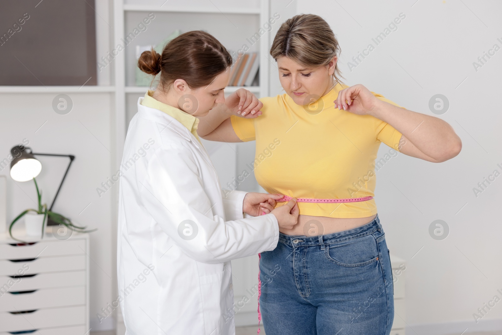 Weight loss. Nutritionist measuring overweight woman's waist with tape in clinic Photo of Weight loss. Nutritionist measuring overweight woman's waist with tape in clinic