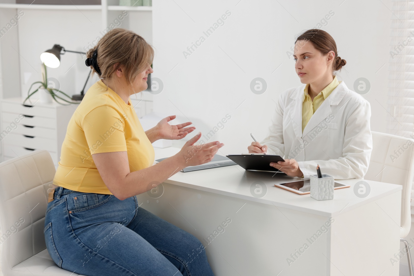 Weight loss. Nutritionist consulting overweight woman at white desk in clinic Photo of Weight loss. Nutritionist consulting overweight woman at white desk in clinic