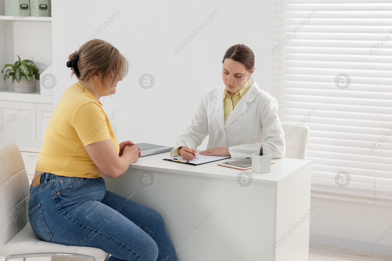 Weight loss. Nutritionist consulting overweight woman at white desk in clinic Photo of Weight loss. Nutritionist consulting overweight woman at white desk in clinic