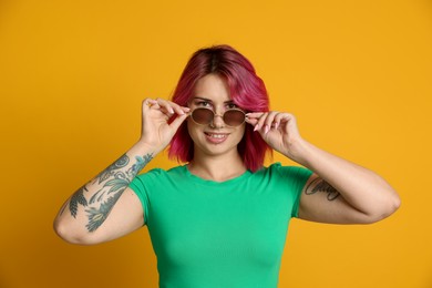 Photo of Beautiful woman with pink dyed hair in sunglasses on yellow background