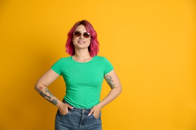 Photo of Beautiful woman with pink dyed hair in sunglasses on yellow background, space for text