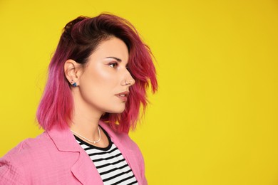 Photo of Beautiful woman with pink dyed hair on yellow background, space for text