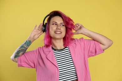 Photo of Beautiful woman with pink dyed hair listening to music on yellow background