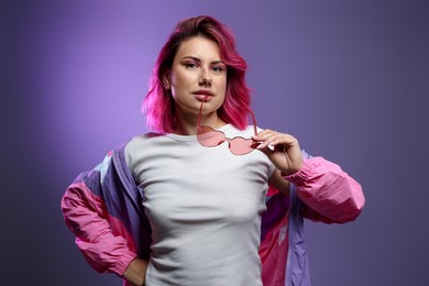 Photo of Beautiful woman with pink dyed hair and sunglasses on violet gradient background
