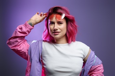 Photo of Beautiful woman with pink dyed hair and sunglasses on violet gradient background