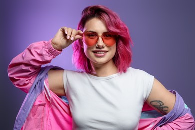 Photo of Beautiful woman with pink dyed hair in sunglasses on violet gradient background