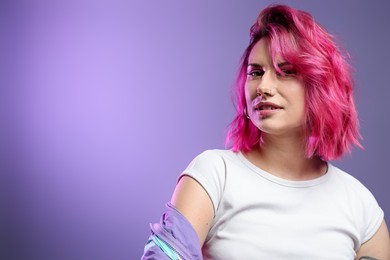 Photo of Beautiful woman with pink dyed hair on violet background, space for text