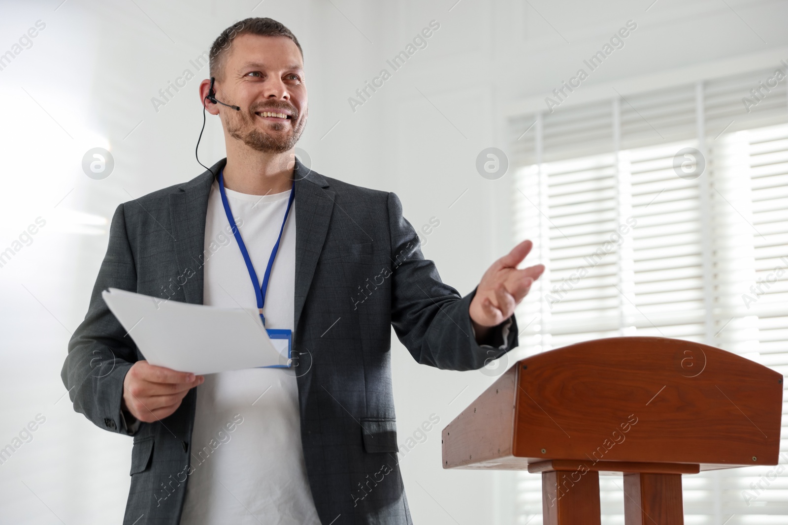 Man giving public speech with microphone at lectern indoors Photo of Man giving public speech with microphone at lectern indoors