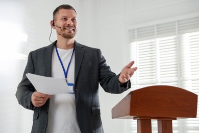 Photo of Man giving public speech with microphone at lectern indoors