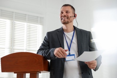 Photo of Man giving public speech with microphone at lectern indoors