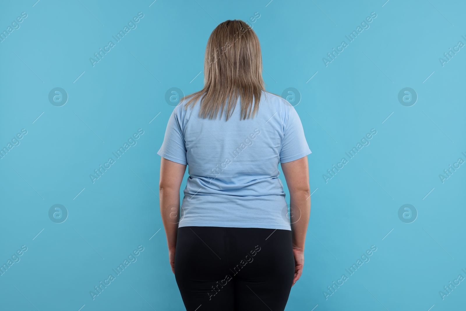 Weight loss. Plus size woman on light blue background, back view Photo of Weight loss. Plus size woman on light blue background, back view