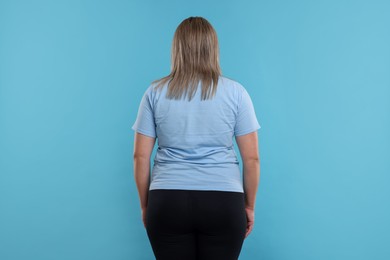 Photo of Weight loss. Plus size woman on light blue background, back view