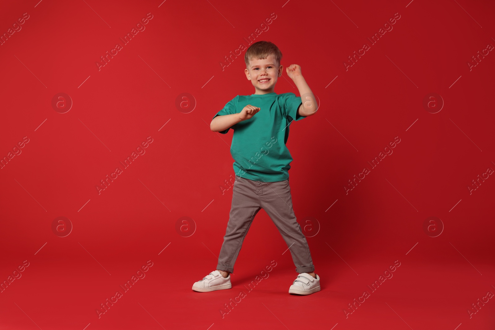 Happy little boy dancing on red background, space for text Photo of Happy little boy dancing on red background, space for text