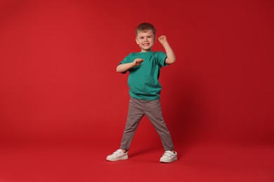 Photo of Happy little boy dancing on red background, space for text
