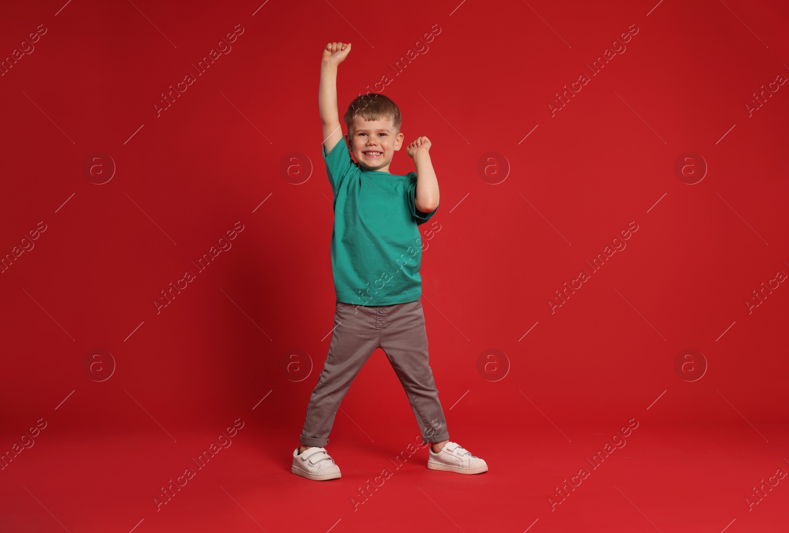 Happy little boy dancing on red background, space for text Photo of Happy little boy dancing on red background, space for text