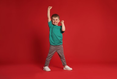 Photo of Happy little boy dancing on red background, space for text