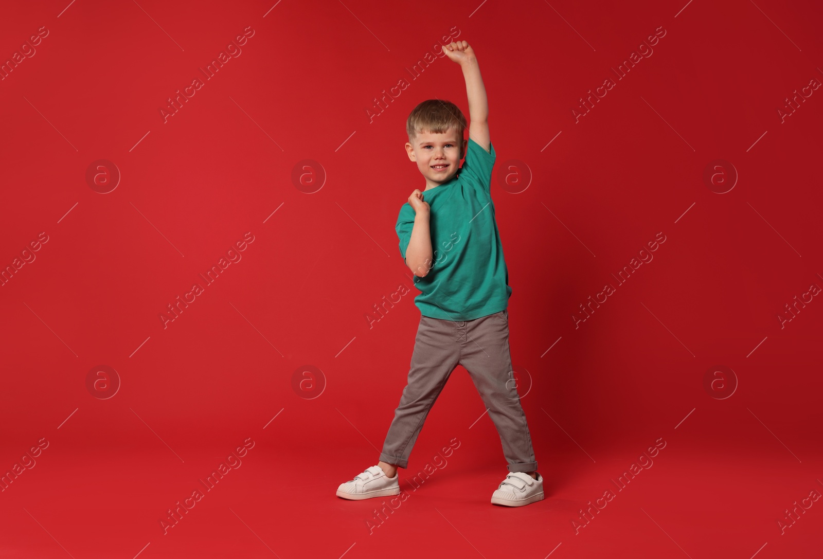 Happy little boy dancing on red background, space for text Photo of Happy little boy dancing on red background, space for text