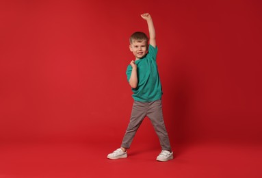 Photo of Happy little boy dancing on red background, space for text