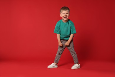 Photo of Happy little boy dancing on red background, space for text